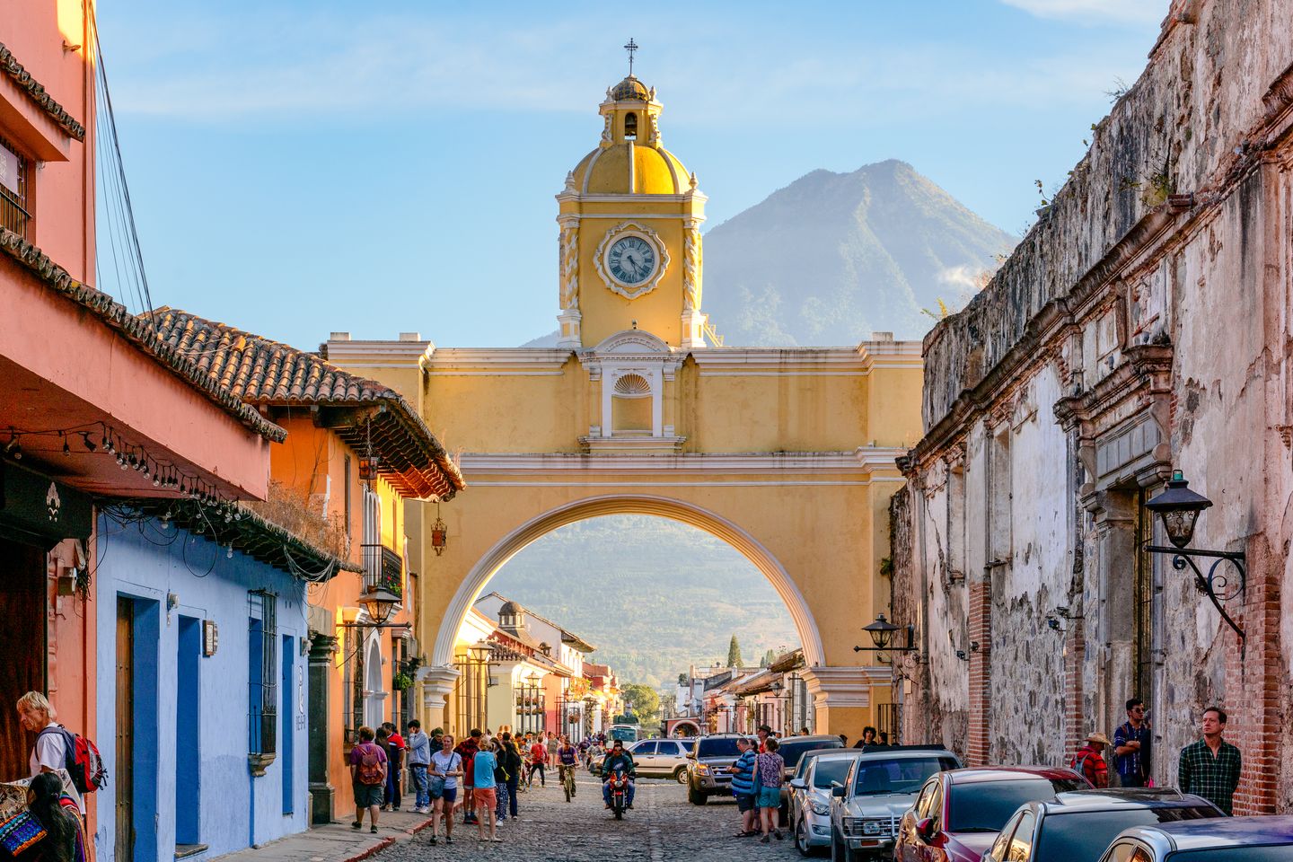The yellow Santa Catalina Arch spanning 5th Avenue North in Antigua Guatemala, with the cone of Volcán de Agua rising behind it under a clear sky