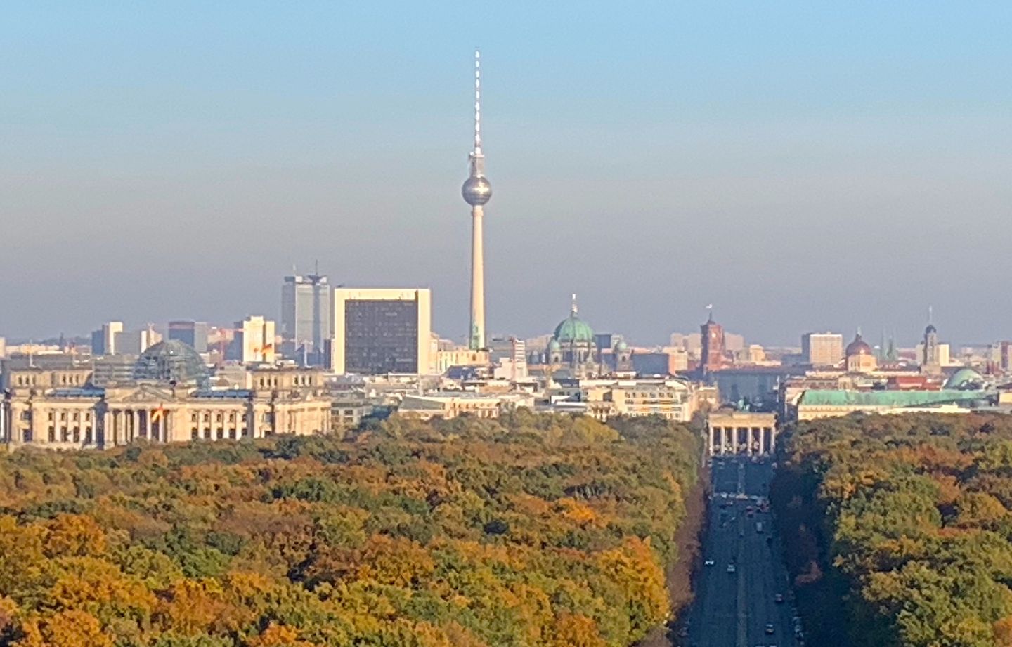 Panoramic view over central Berlin from the Victory Column, with the Reichstag dome, the Berlin Cathedral and the TV Tower visible across the Tiergarten and the rooftops of Mitte