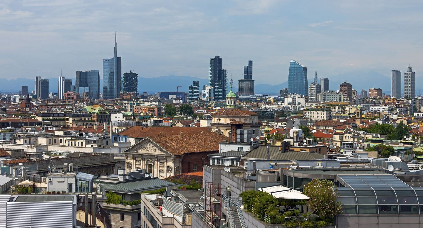 The white marble spires and gilded Madonnina statue of Milan's Duomo seen against the city skyline at dusk