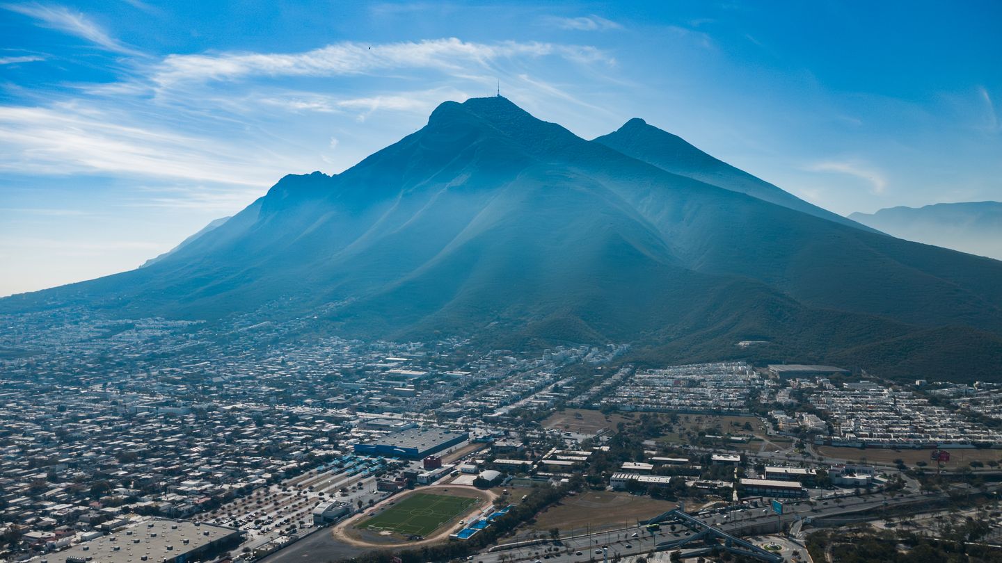 The distinctive twin-peaked silhouette of Cerro de la Silla rising behind the modern skyline and rooftops of Monterrey, Nuevo León, Mexico, seen in late-afternoon light