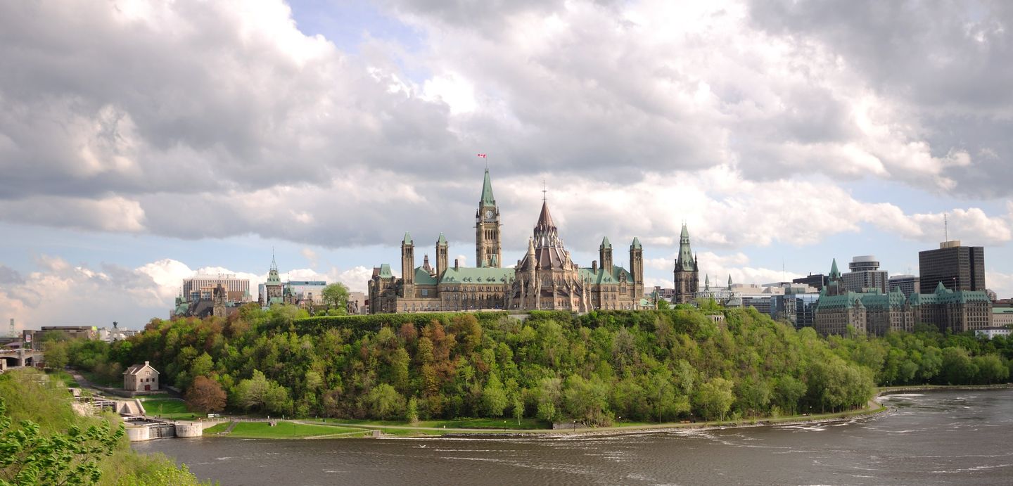 A southward view of Parliament Hill's Gothic Revival towers in Ottawa, photographed from Majors Hill Park with the Rideau Canal's flight of locks visible at left and Place de Ville's tower on the right