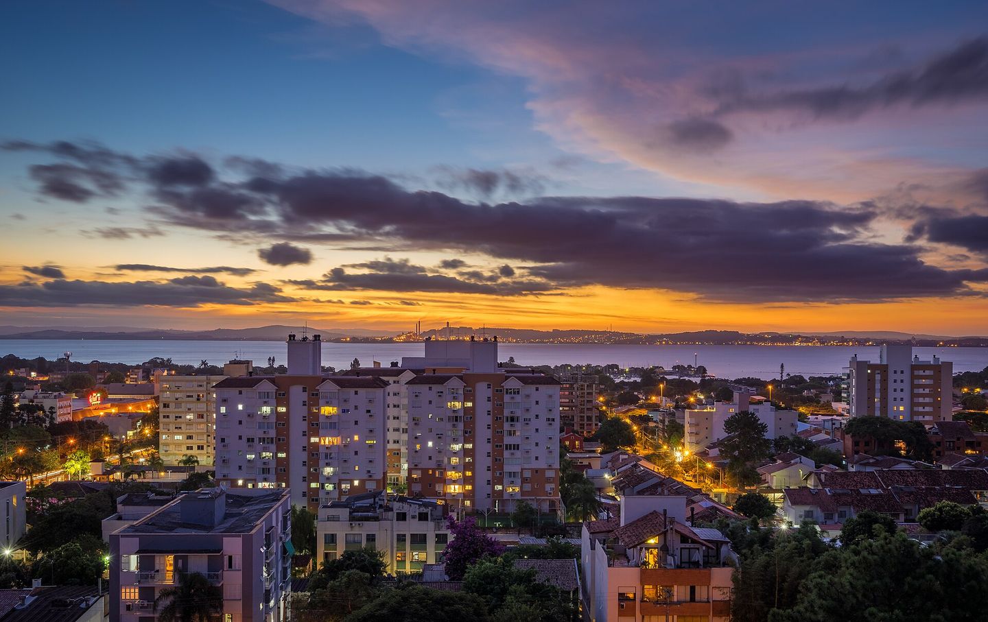 Porto Alegre's skyline lit in deep blue hour light along the Guaíba waterfront, with illuminated towers reflected in the water