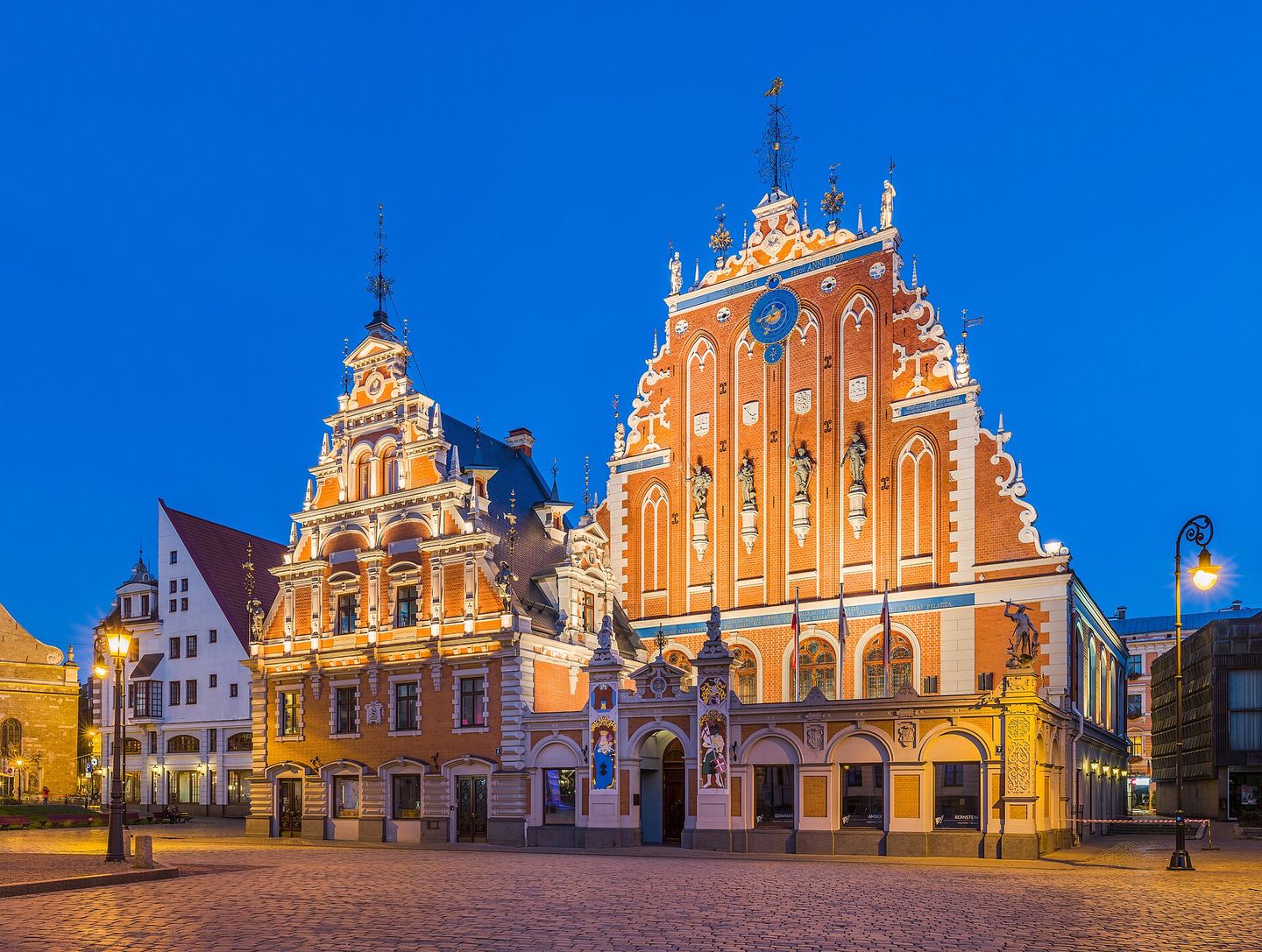 The ornate stepped gables of the House of the Blackheads illuminated at dusk in Riga's Old Town, Latvia, with St. Peter's Church tower rising behind