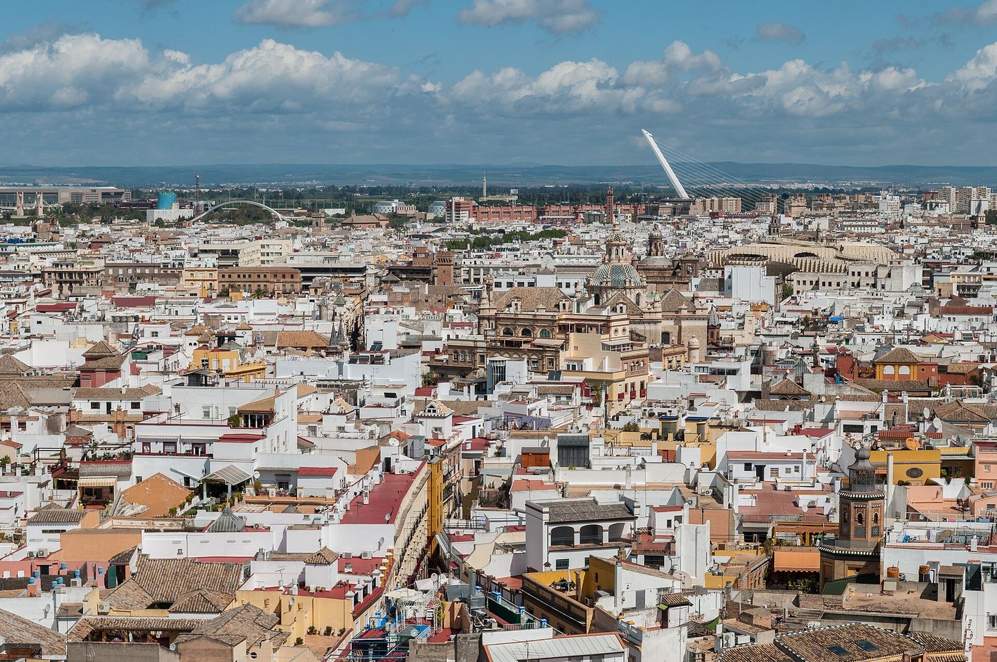 View over the tiled rooftops and whitewashed buildings of central Seville from the top of the Giralda bell tower, with the city spreading toward the hills on the horizon