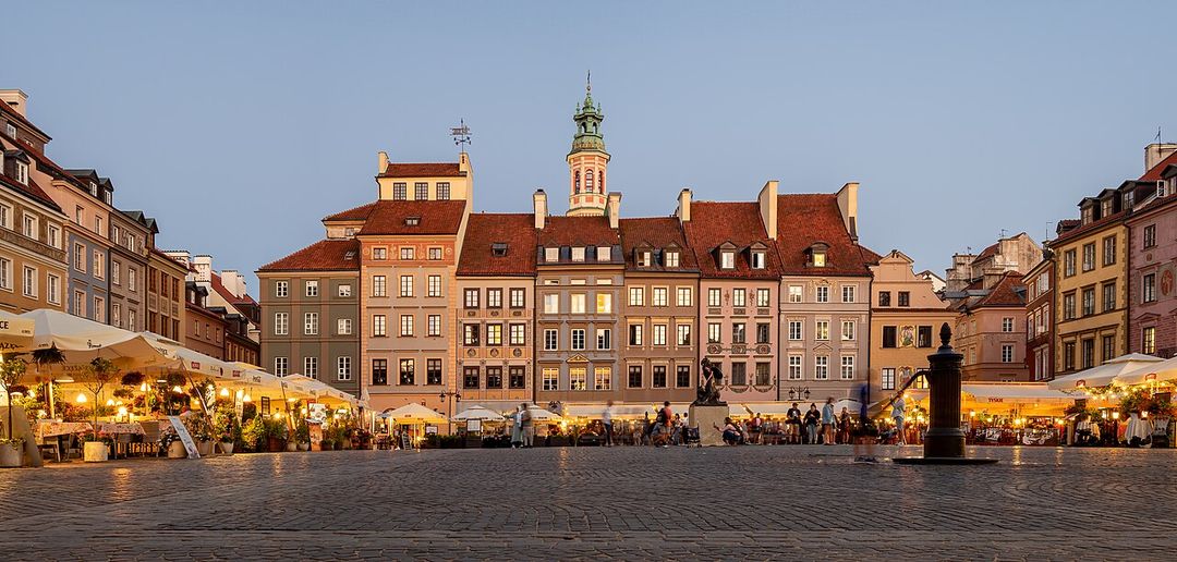 The colourful reconstructed burgher houses and cobbled Old Town Market Square in Warsaw, seen from ground level with cafe tables in the foreground